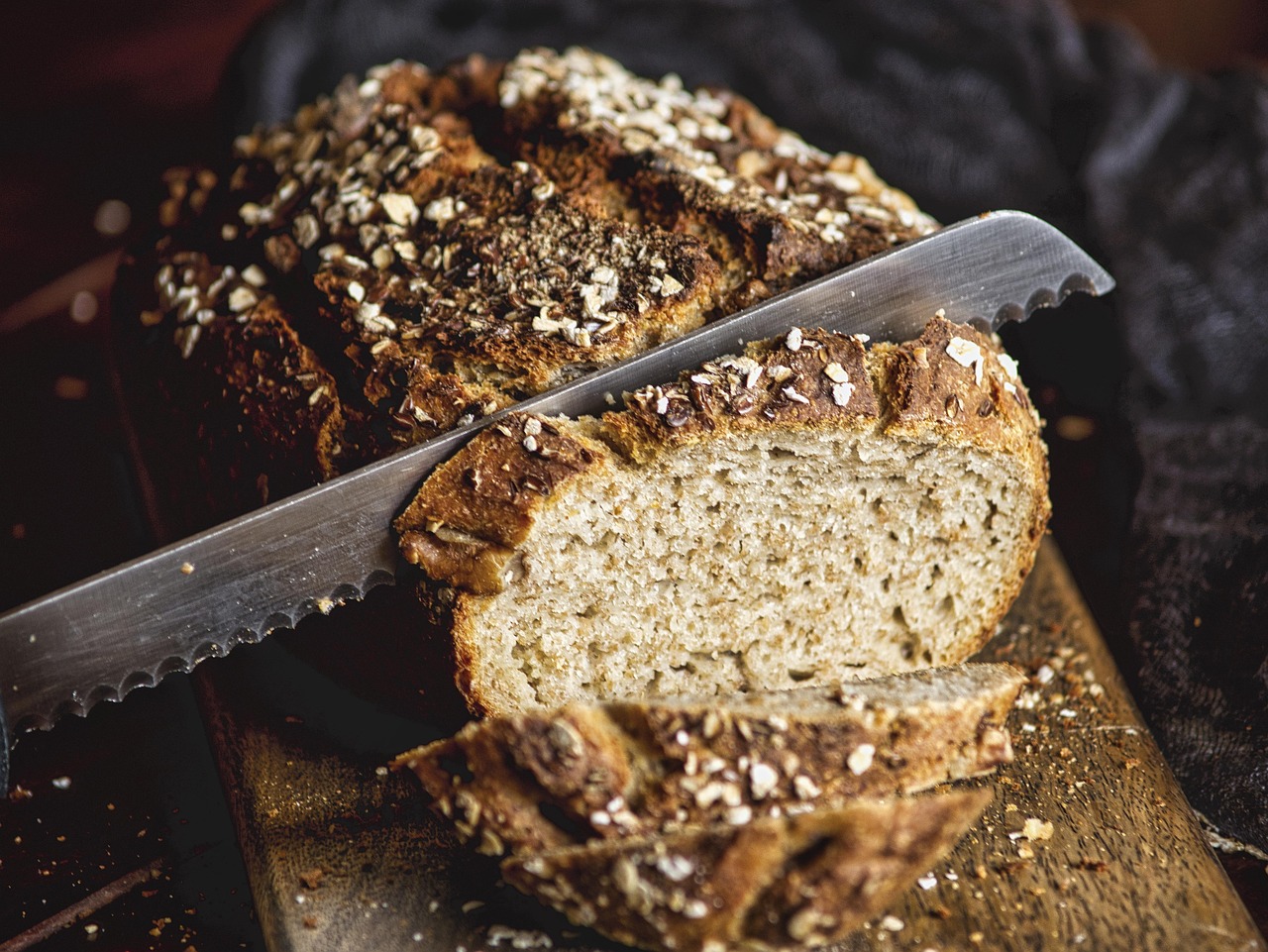 Rustic whole wheat loaf being sliced with a serrated knife.