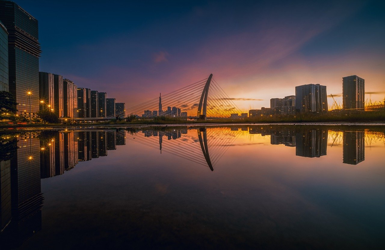 Photo of the Month Winner: Modern cable bridge reflecting in water with a city skyline at sunset (Category: Architecture)